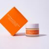 Bright orange dermatology cream packaging on white background for skincare advertisement.